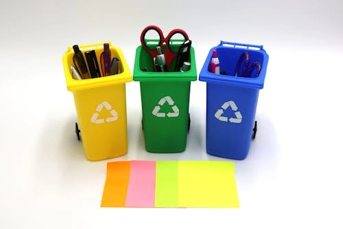 The image shows three recycling bins filled with office supplies