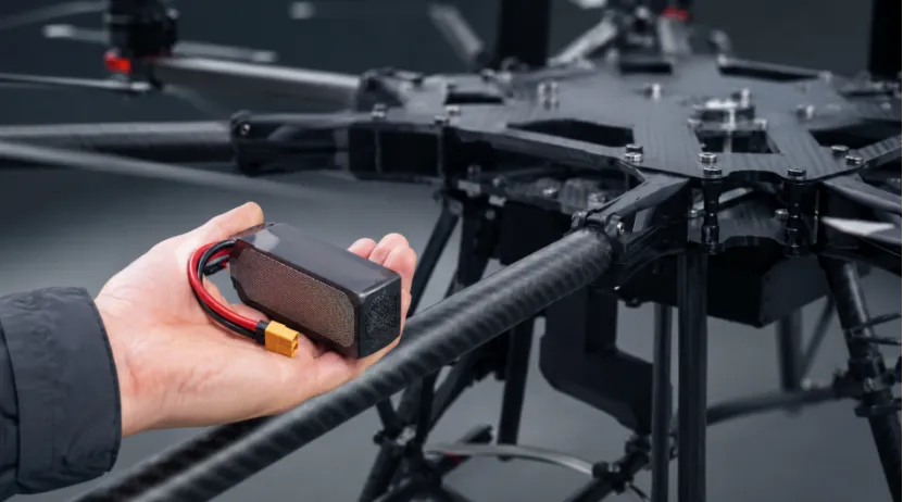 Hand holding a compact high-energy-density drone battery next to an industrial UAV